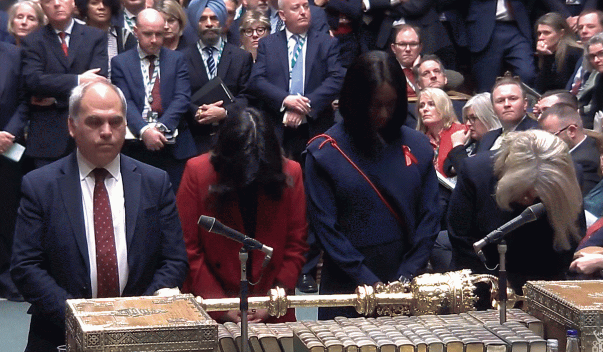 Four MPs stand at a table with heads bowed.