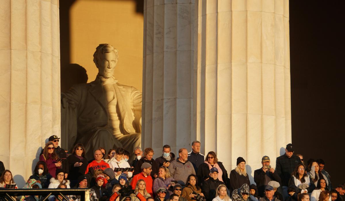 A crowd of people stand in the side steps of the Lincoln Memorial