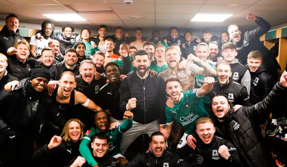 in a dressing room, celebrating footballer crowd together for a photograph.
