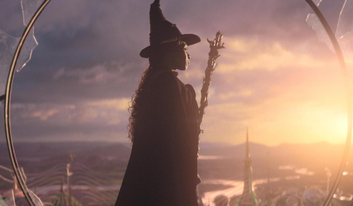 In a still from Wicked, the witch stands and looks to the sunset.