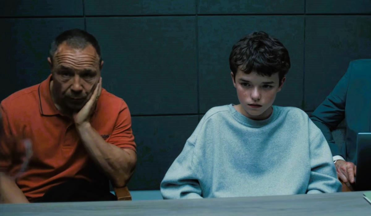 An unhappy father sits next to a scared son in a police interview room.
