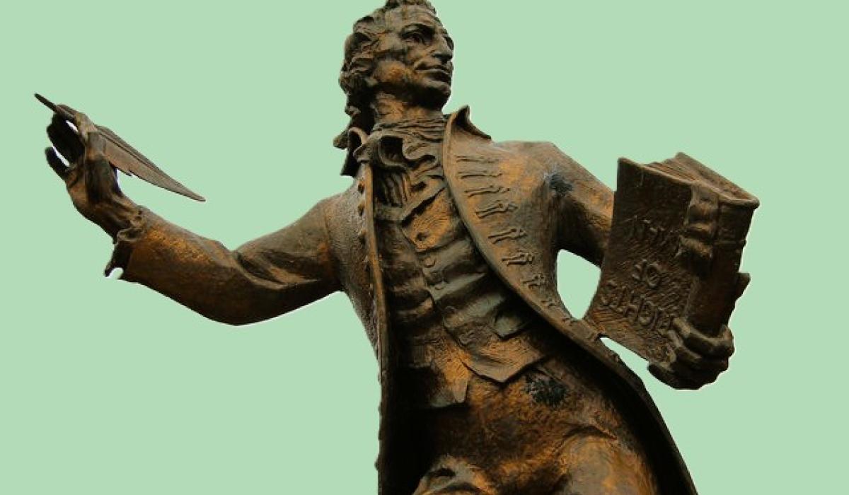 A statue of a 18th century man holding a pen and a book.