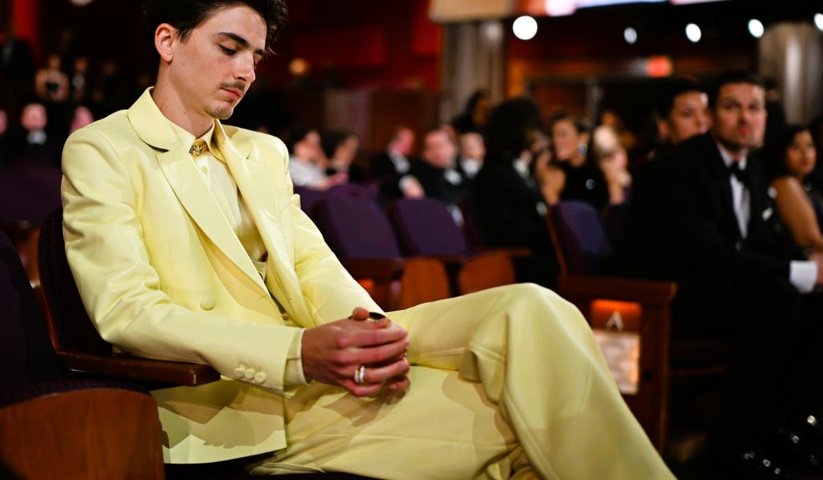 Timothee Chalamet, wearing  light yellow suit reposes in a seat a the Oscars, clasping his hands, his eyes closed.