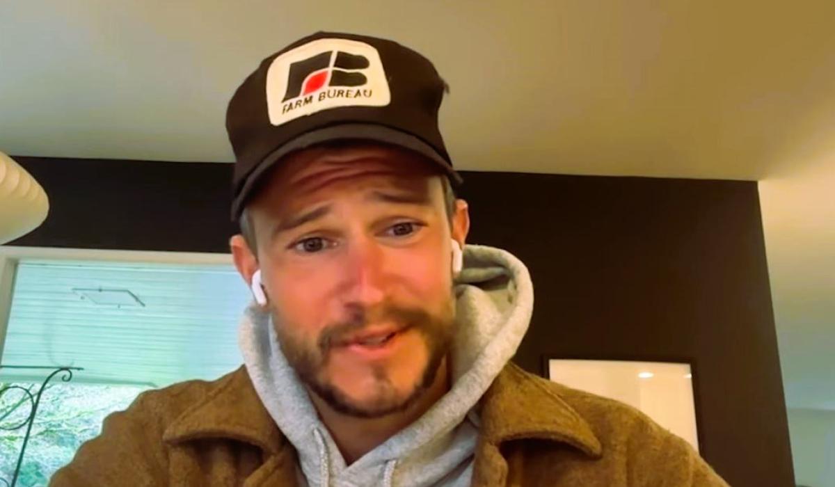 A podcast guest, wearing a baseball hat, looks at a screen.