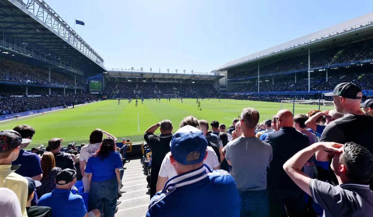 Football fans wearing blue stand and watch a match in a stadium.
