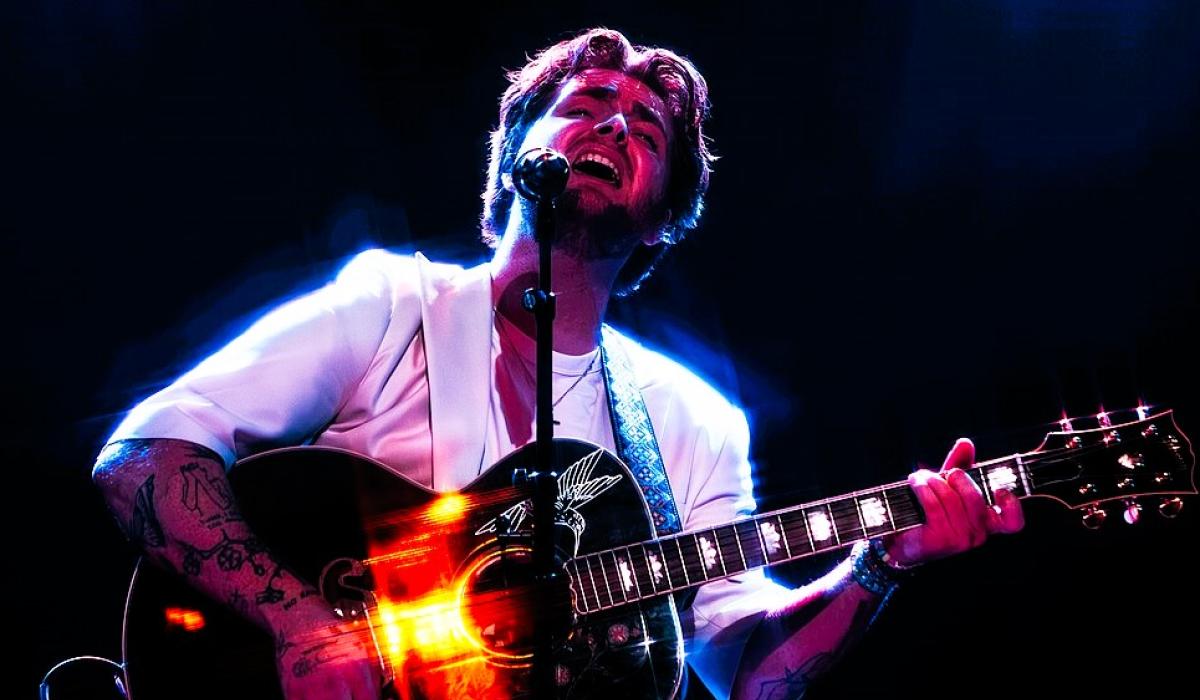 A singer holding a guitar raises his head with closed eyes.