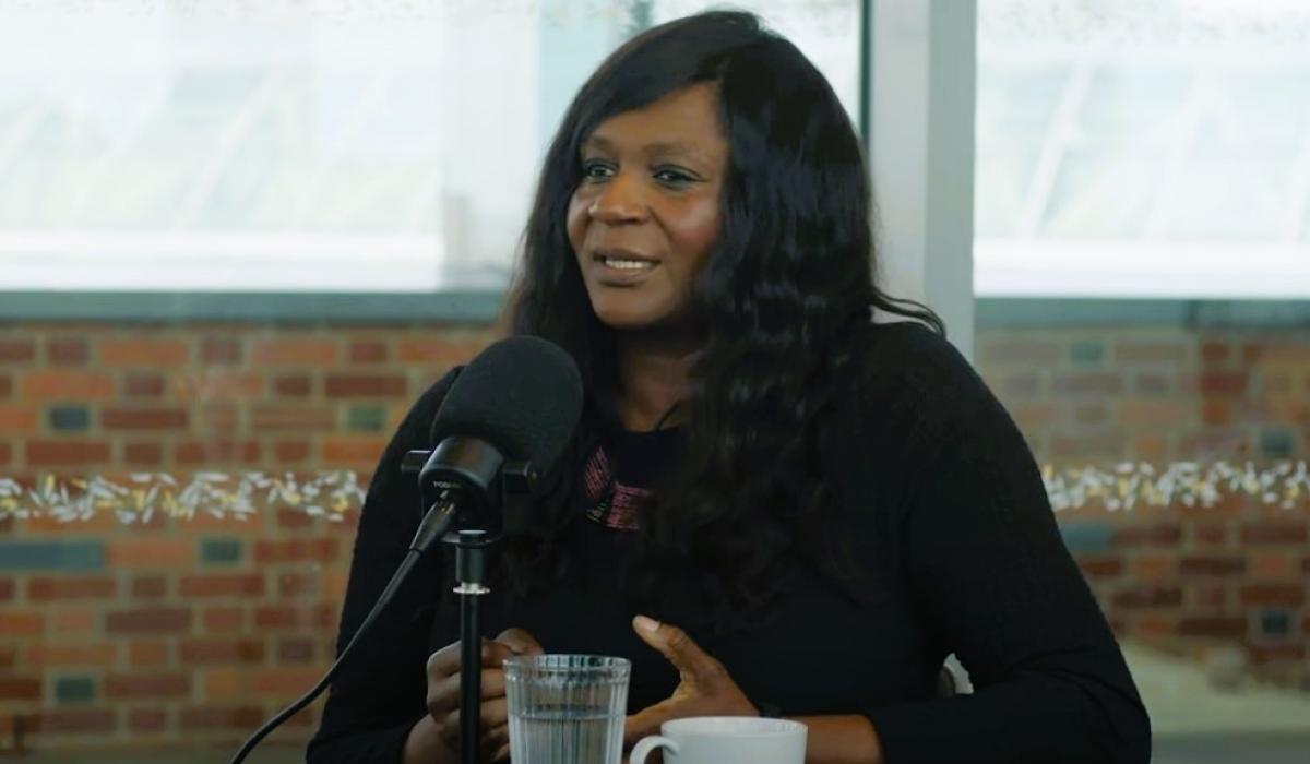 A podcast guest sits in front of a mic talking and gesturing with her hands.