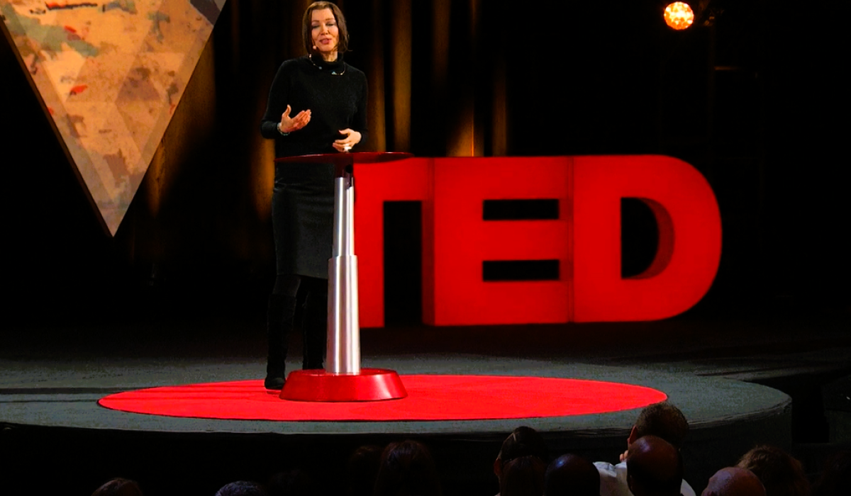 A speaker stands beside a podium in front of a TED sign.