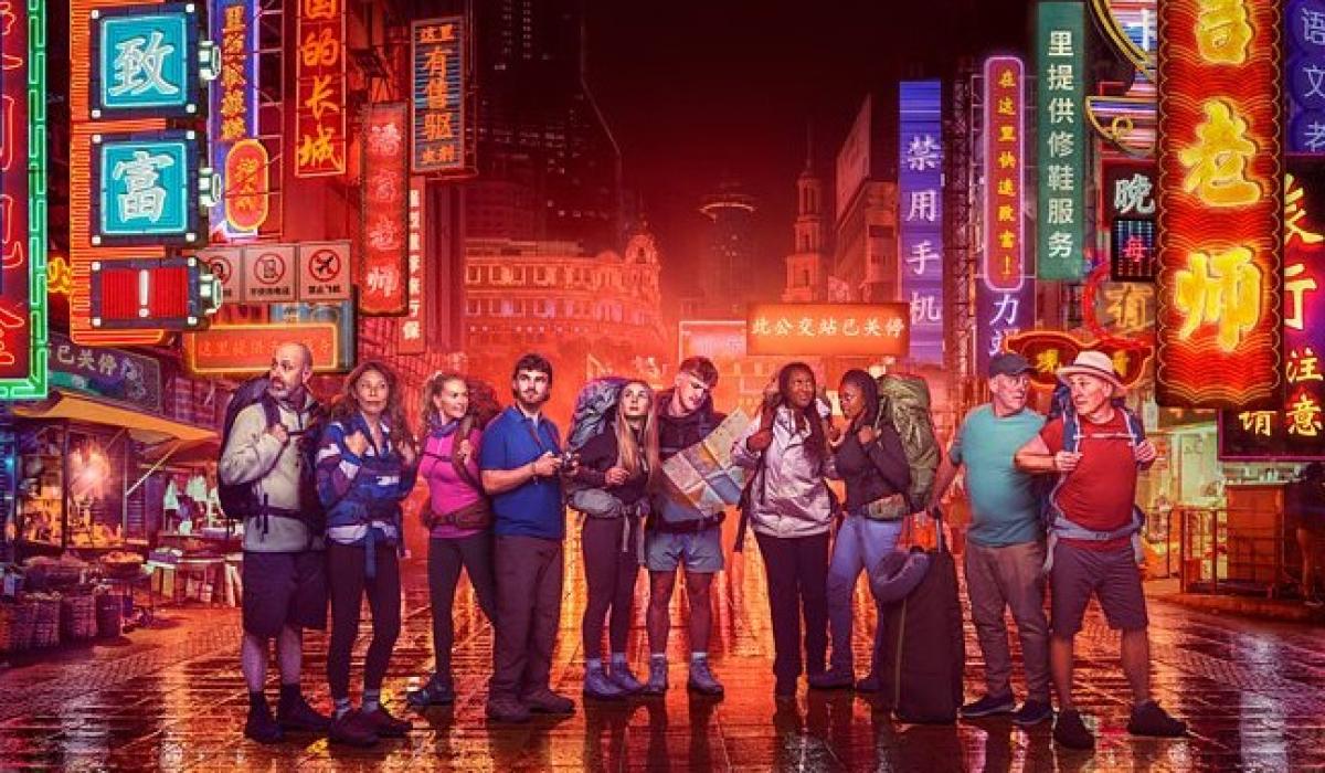 Contestants in Race Across the world stand in front of neon-lit Chinese street scene