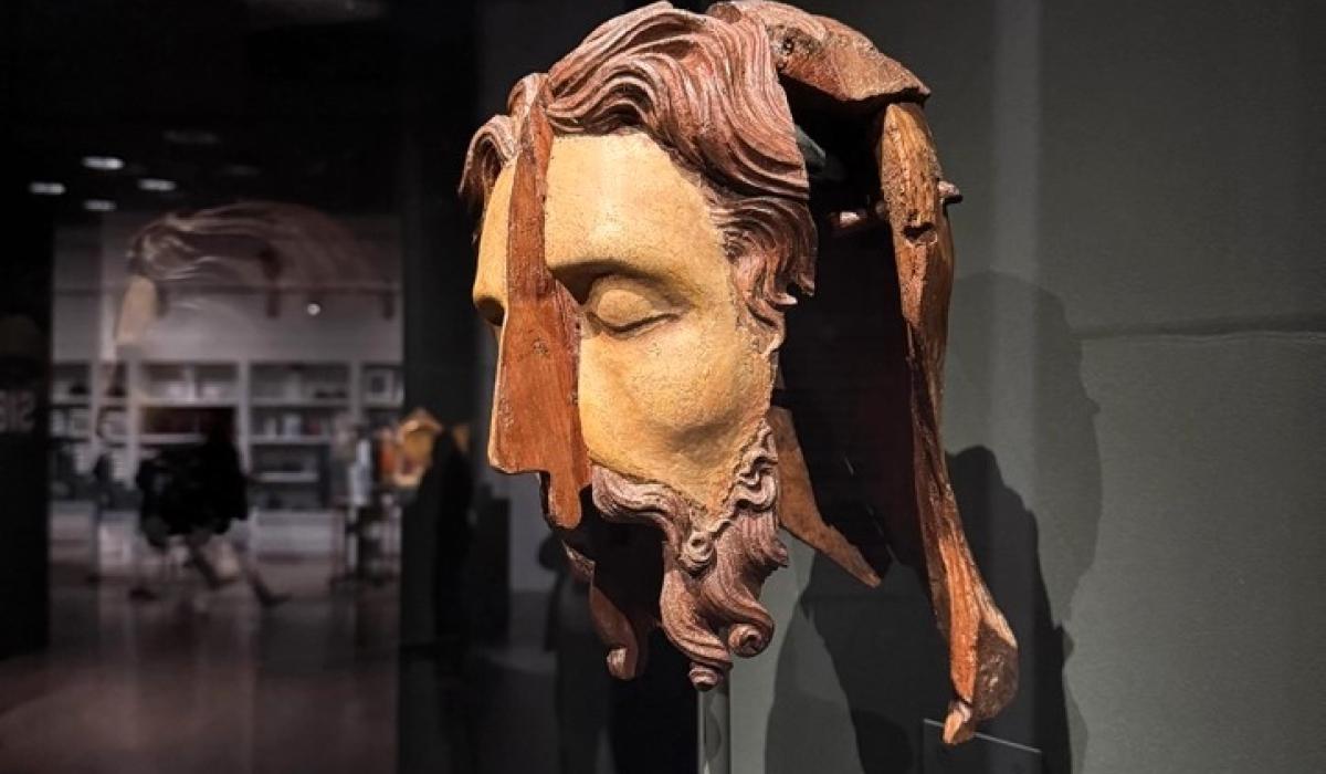 A split wooden sculpted head stands in an exhibition.