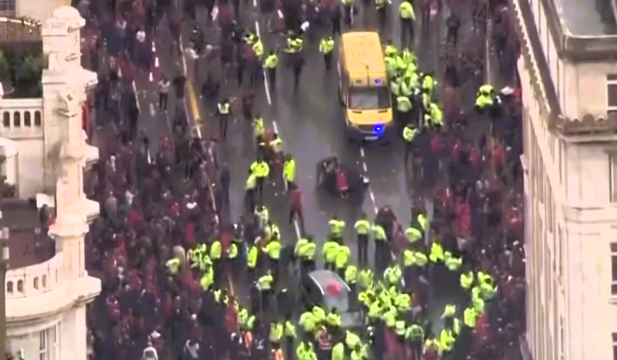 Aerial view of a yellow-jacketed police forming a cordon within a crowd.