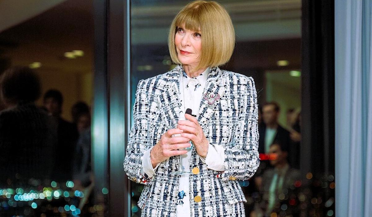 Anna  Wintour stands holding a small mic.