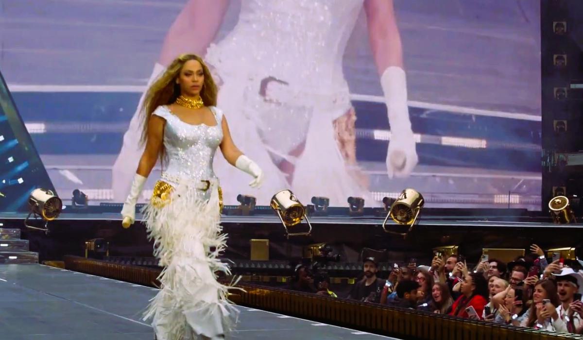 Beyonce marches along a stage catwalk as photographers stare from below.