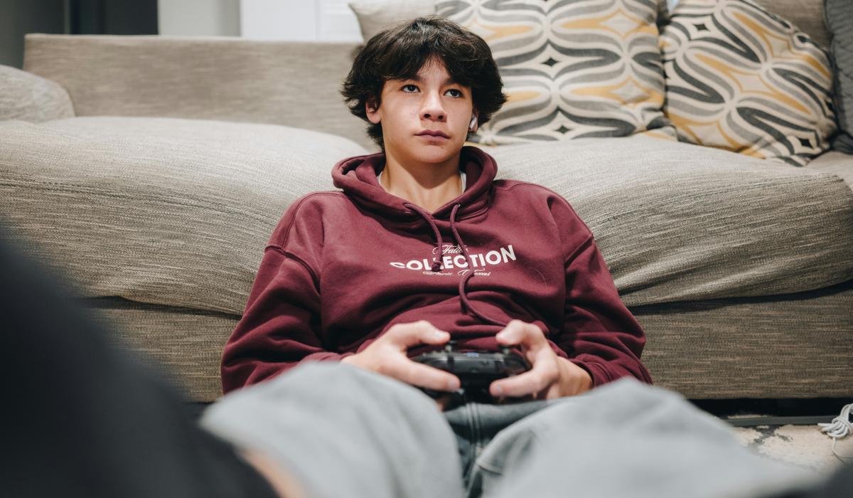 A teenager slumped against a sofa plays a video game