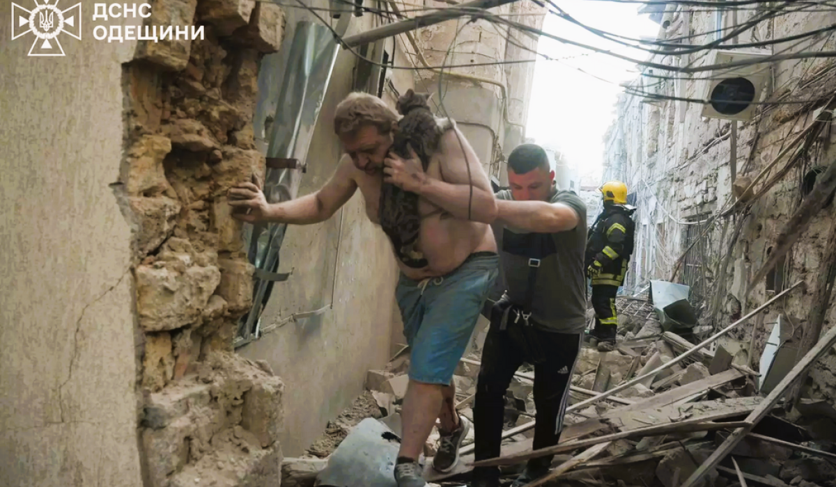 Amid a bombed alley, a victim is helped to walk by a rescue worker