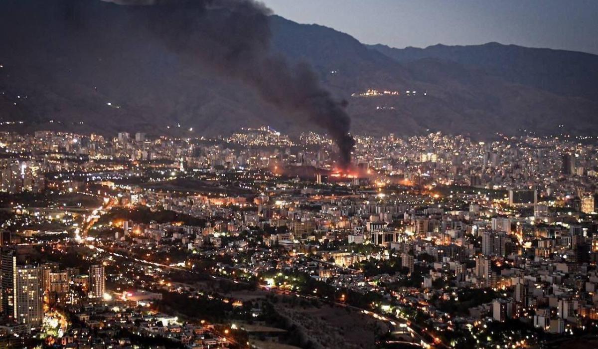 Smoke rises from the site of a bomb amid a high wide view of a city at twlight