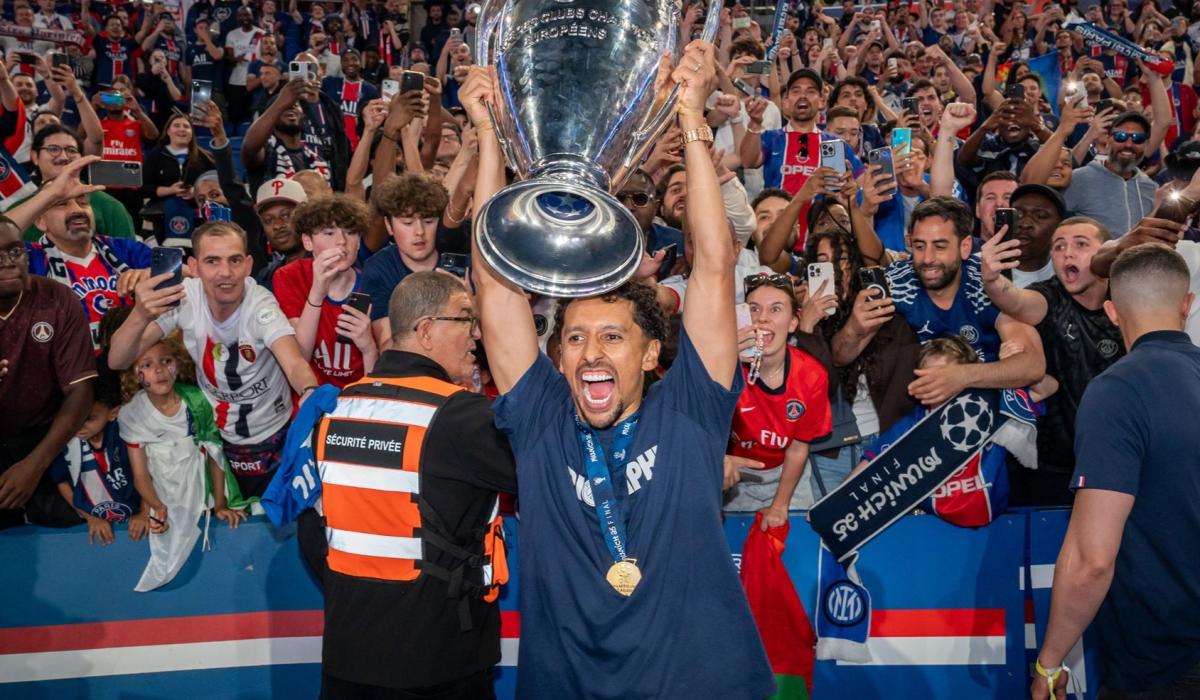 A footballer holds up the European cup, behind him fans are jubillant.