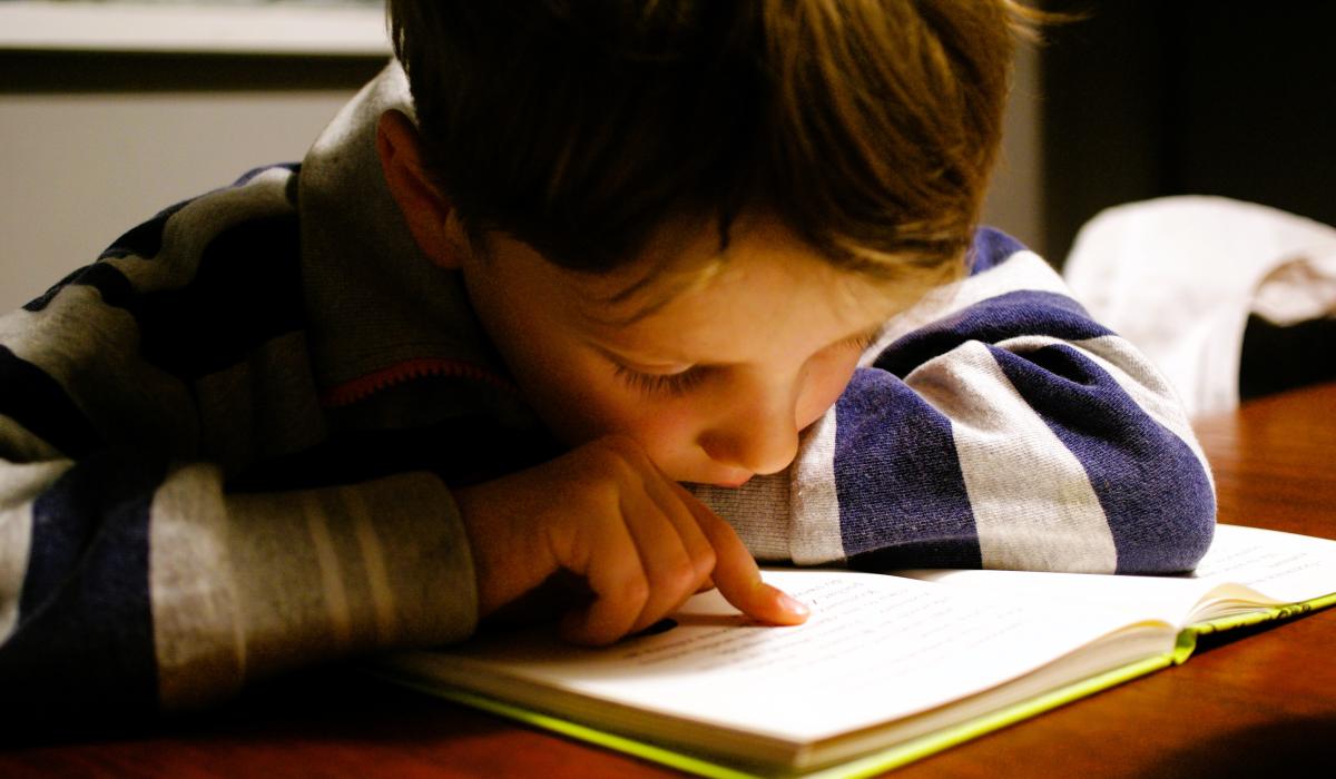 A young boy pores over a book tracing the lines with a finger.