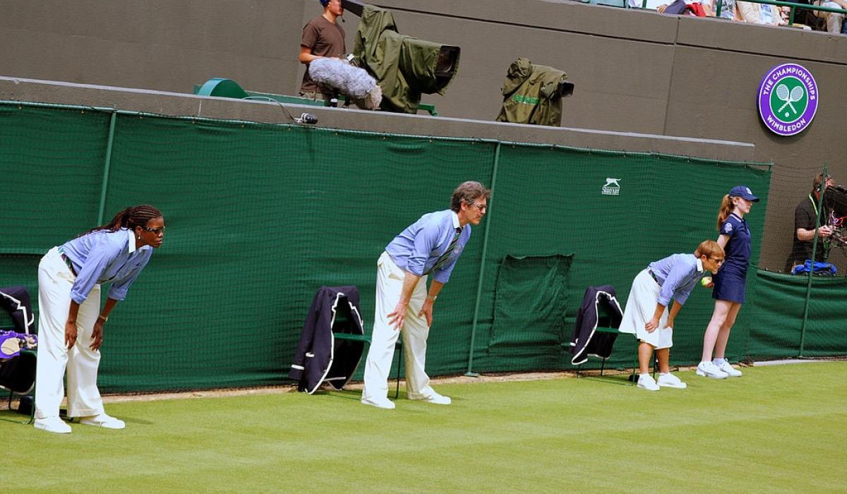 Tennis line judges stand and lean forward with hands on knees