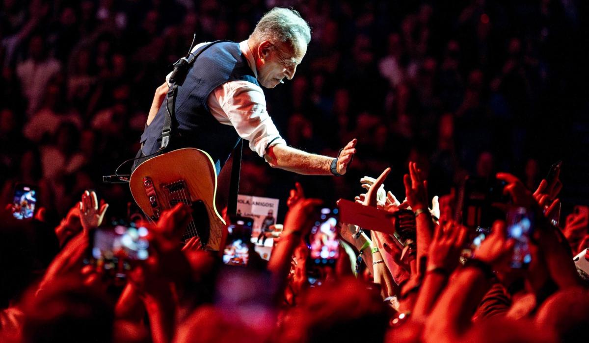 Bruce Springsteen crouches down and holds a hand out to a sea of outstretched hands