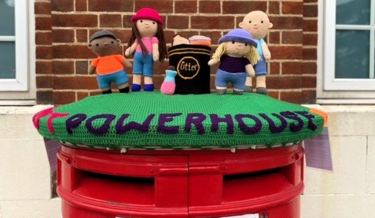 A knitted post box topper shows a group of people and the word powerhouse.