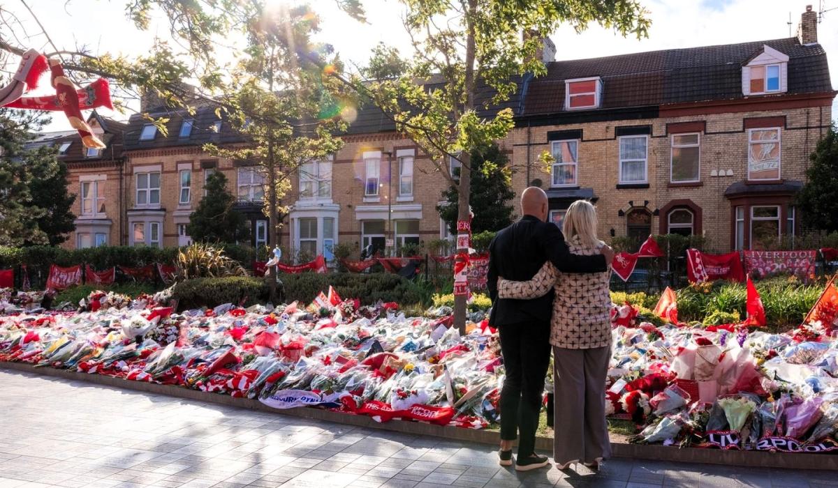 A couple hold each other as they look at floral tributes on the ground