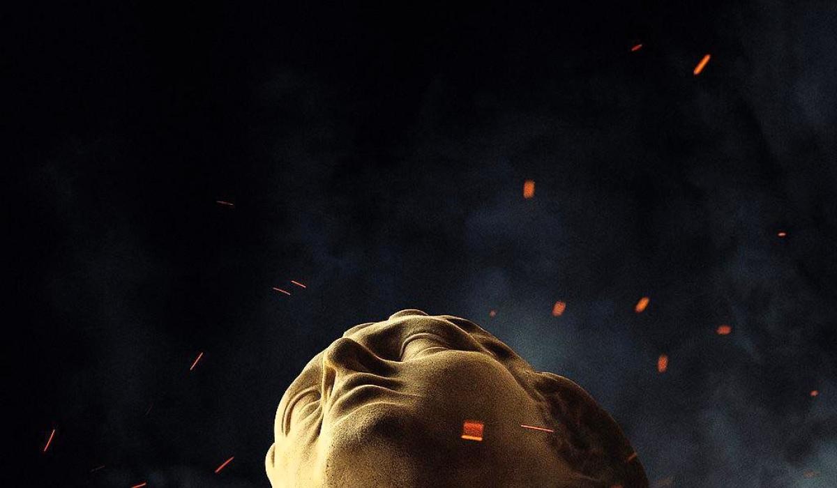 the head of a classical statue looks up amid embers around it.