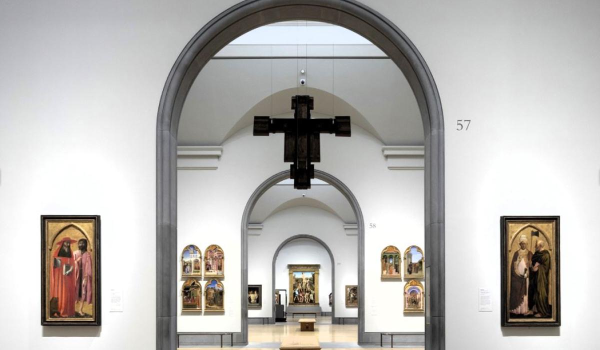 An art gallery arch reveals a suspended crucifix and other paintings in a distant room