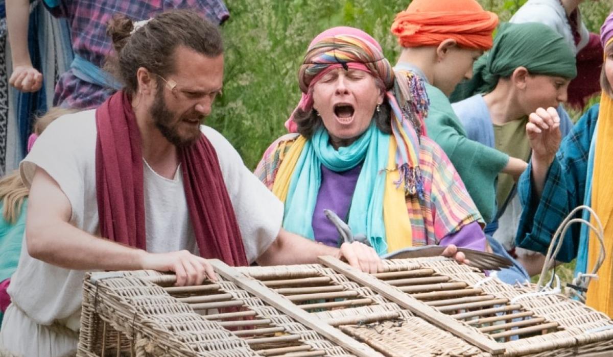 An outdoor theatrical setting shows Jesus with a basket.