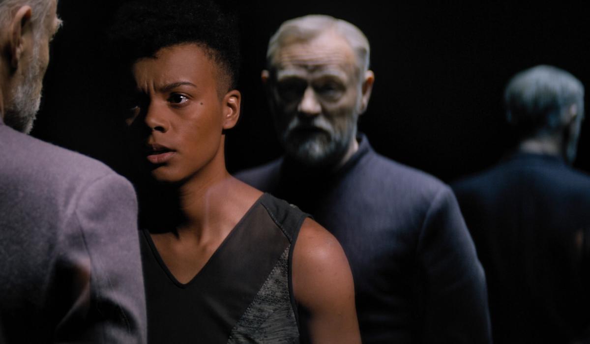 A woman confronts a man whose clone stands behind her.