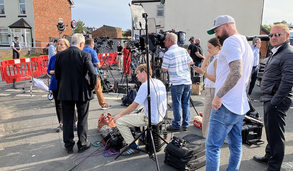 A media pack await a press conference in a street.