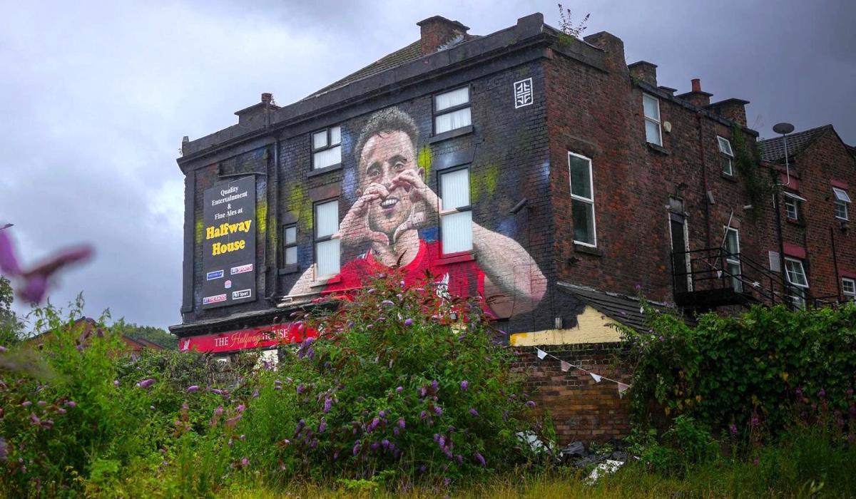 A mural on a side of a pub shows a footballer making a heart sign.