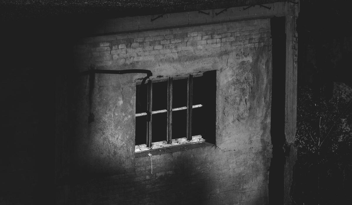 A barred window sits in a dark brick wall.