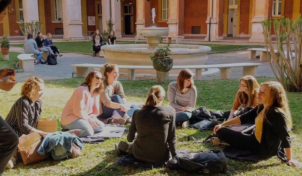 Students sit on the grass in front of a fountain.