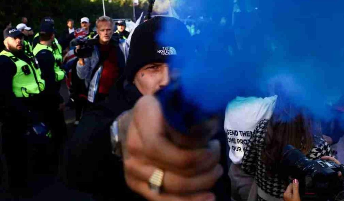 A protestor holds a blue smoke canister towards the camera lens.