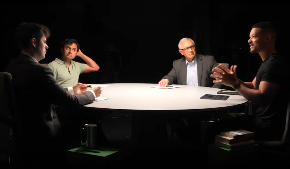 A spotlit round table with podcast guests around it.