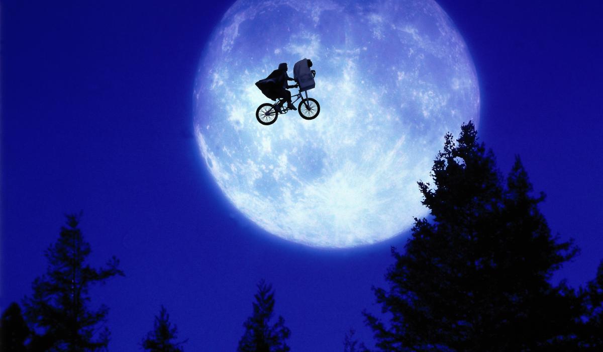 A child and E.T. ride a BMX bike across a moon lit sky.