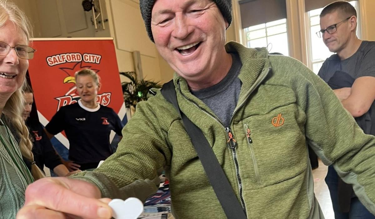 A man presents a heart shaped paper token towards the camera