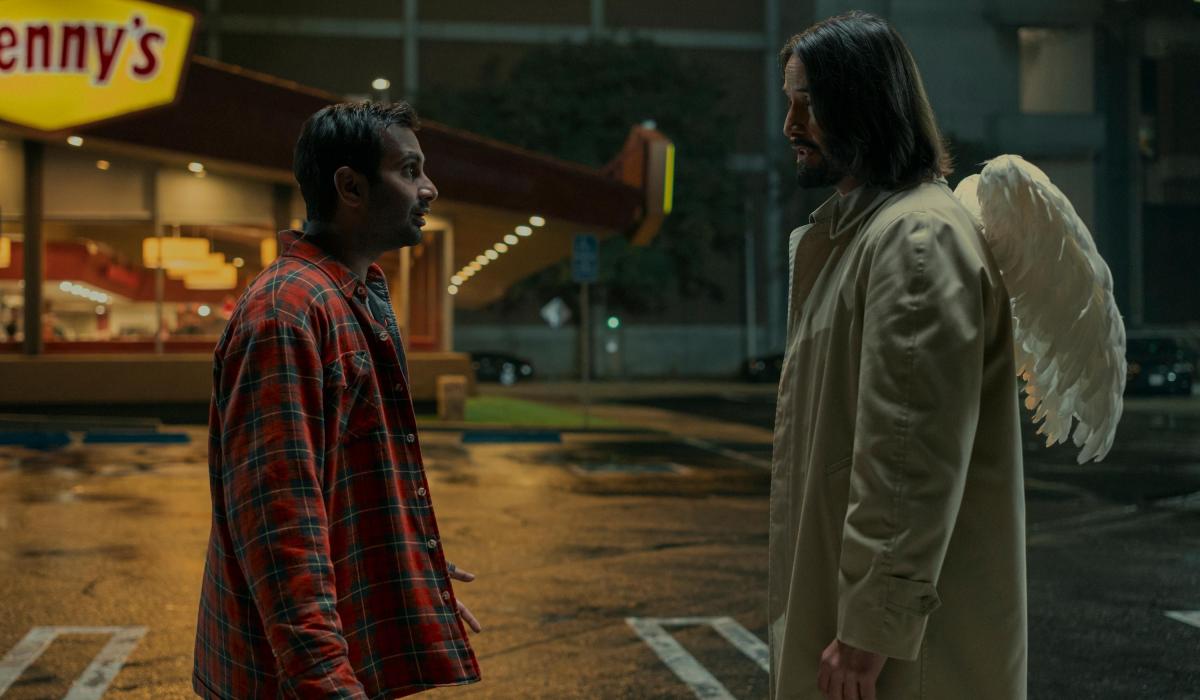 A film character talks to an angel in the street who has wings on the back of his coat.