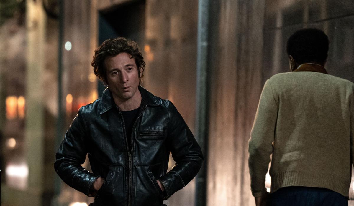 An actor playing Bruce Springsteen walks down a dark street, hands in jacket pocket.