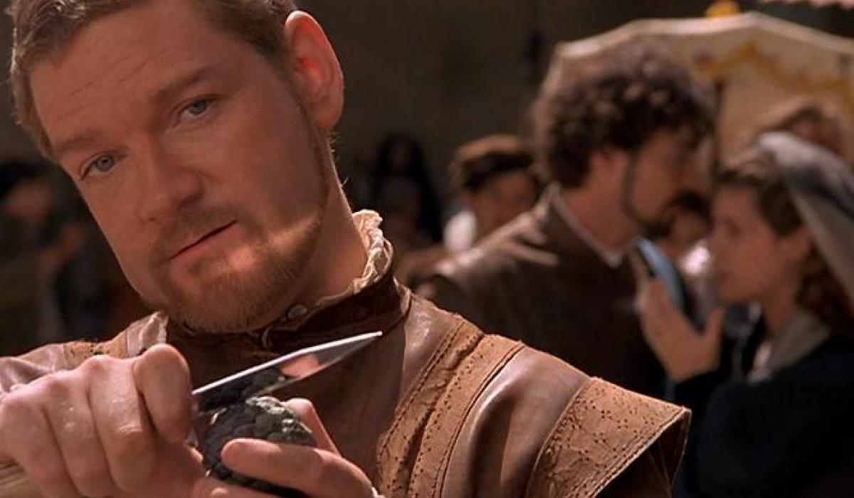 An Elizabethan man holds a dagger up while grinning.