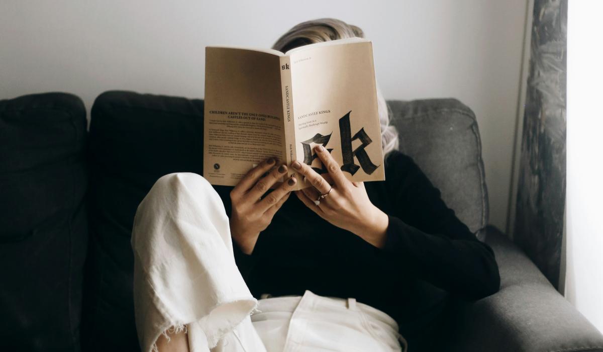   A reader sits on a sofa with a raised leg and holds a book