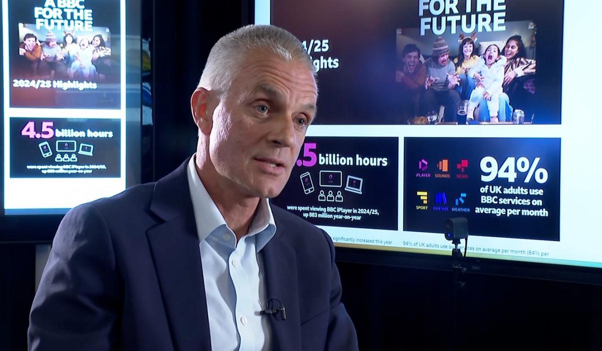 TIm Davie, sits in an interview in front of screens showing facts about the BBC