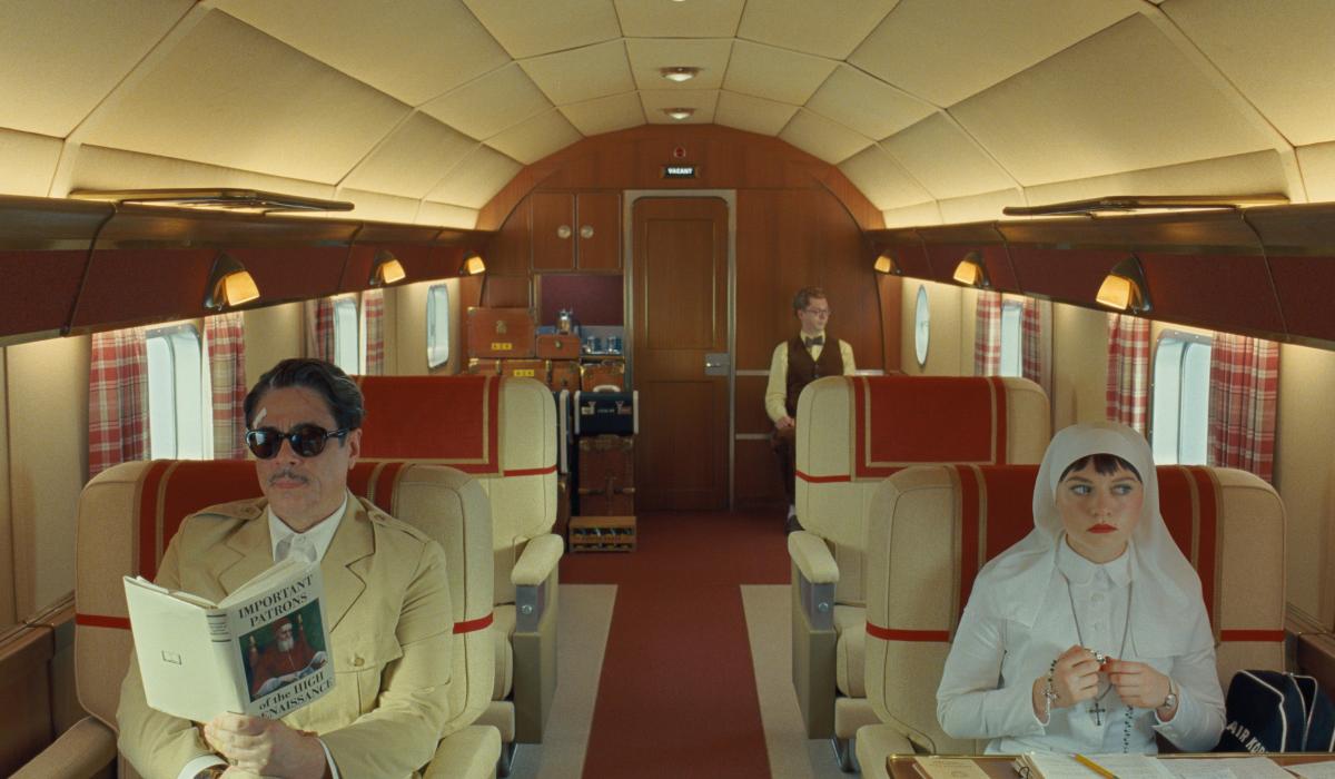 Characters from a Wes Anderson film sit in a stylish plane interior.