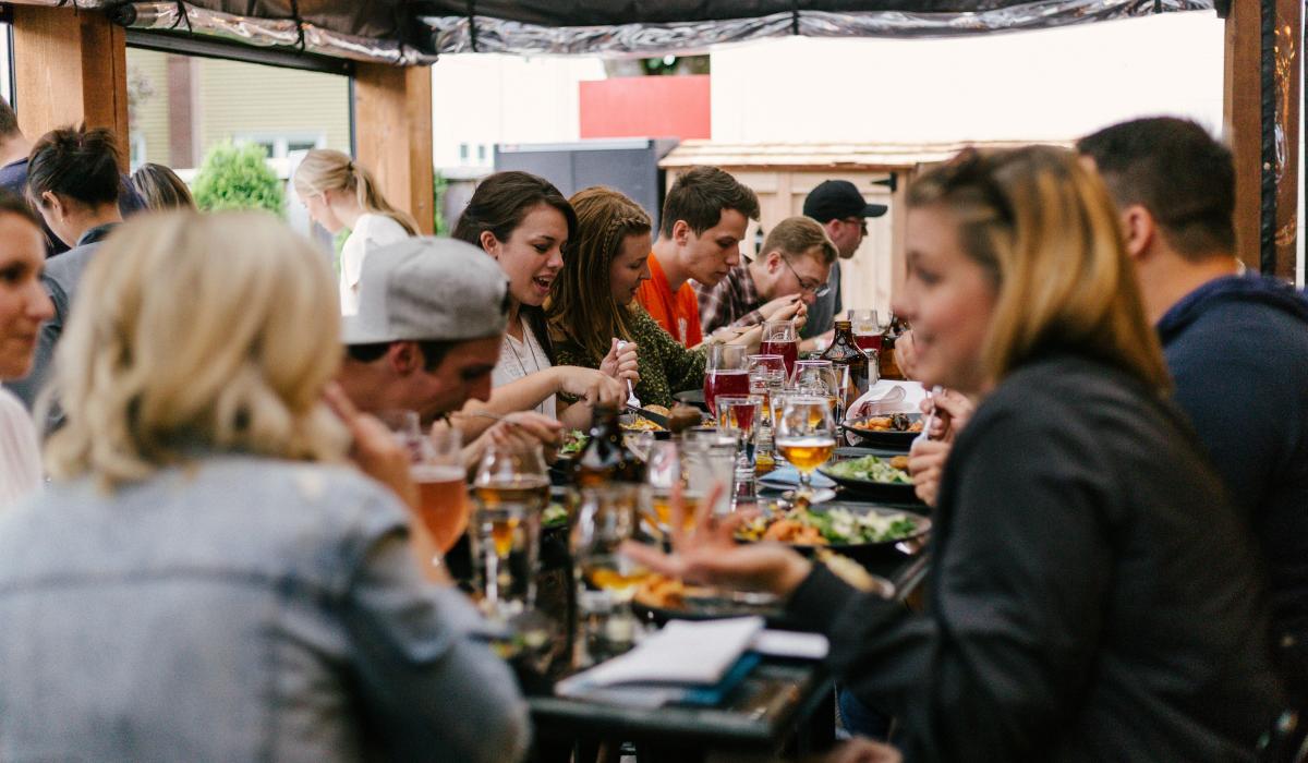 A group of friends sit arouns a large table eating together.