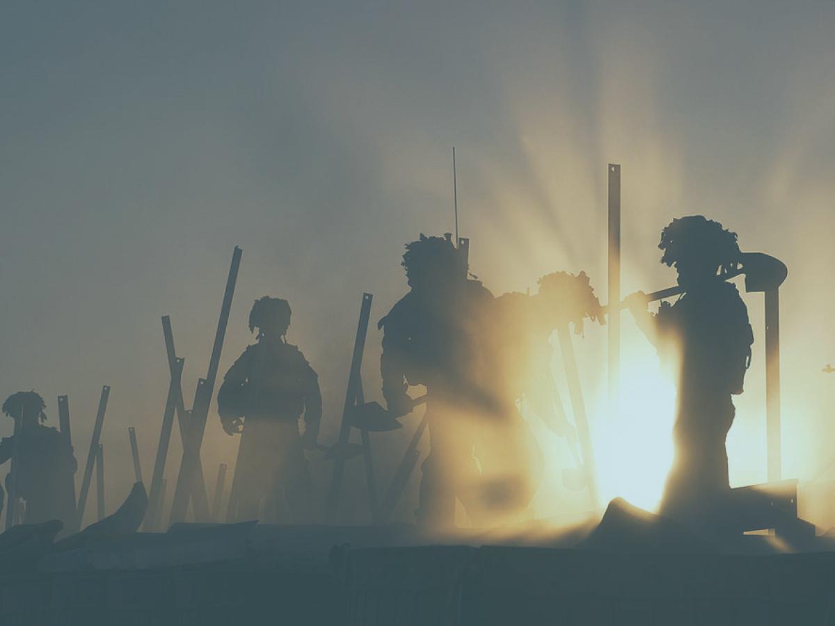 Soldiers silhouetted by dust and sunshine work at a fence with tools.