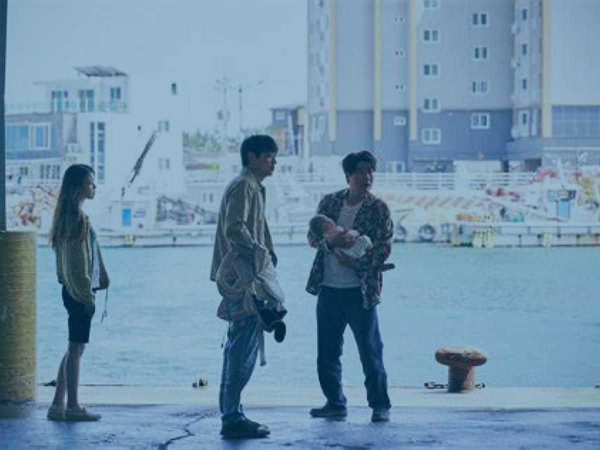 Three people, one carrying a baby, stand on a dock side at a harbour