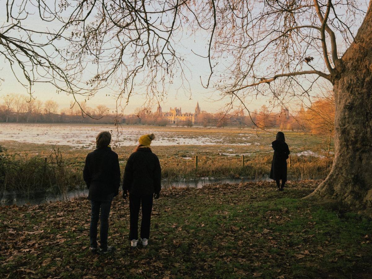 On the edge of wintery meadow a couple and a stranger stand apart.