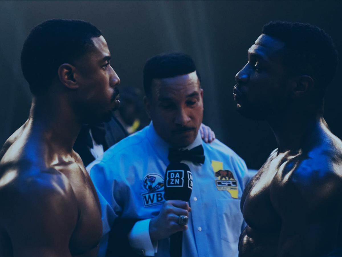 In a boxing ring, an umpire stands between two boxers who stare hard at each other.