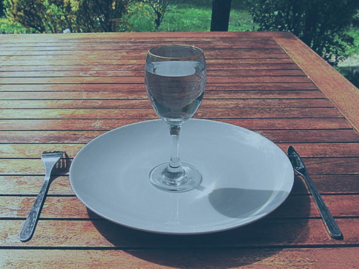 A wine glass of water sits on an empty clean plate.
